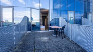 A modern outdoor seating area with a table and chairs, a view of the cityscape through large windows, and a glass door leading to an interior space. - B&B HOTEL Expo Verona Villafranca (Villafranca di Verona)