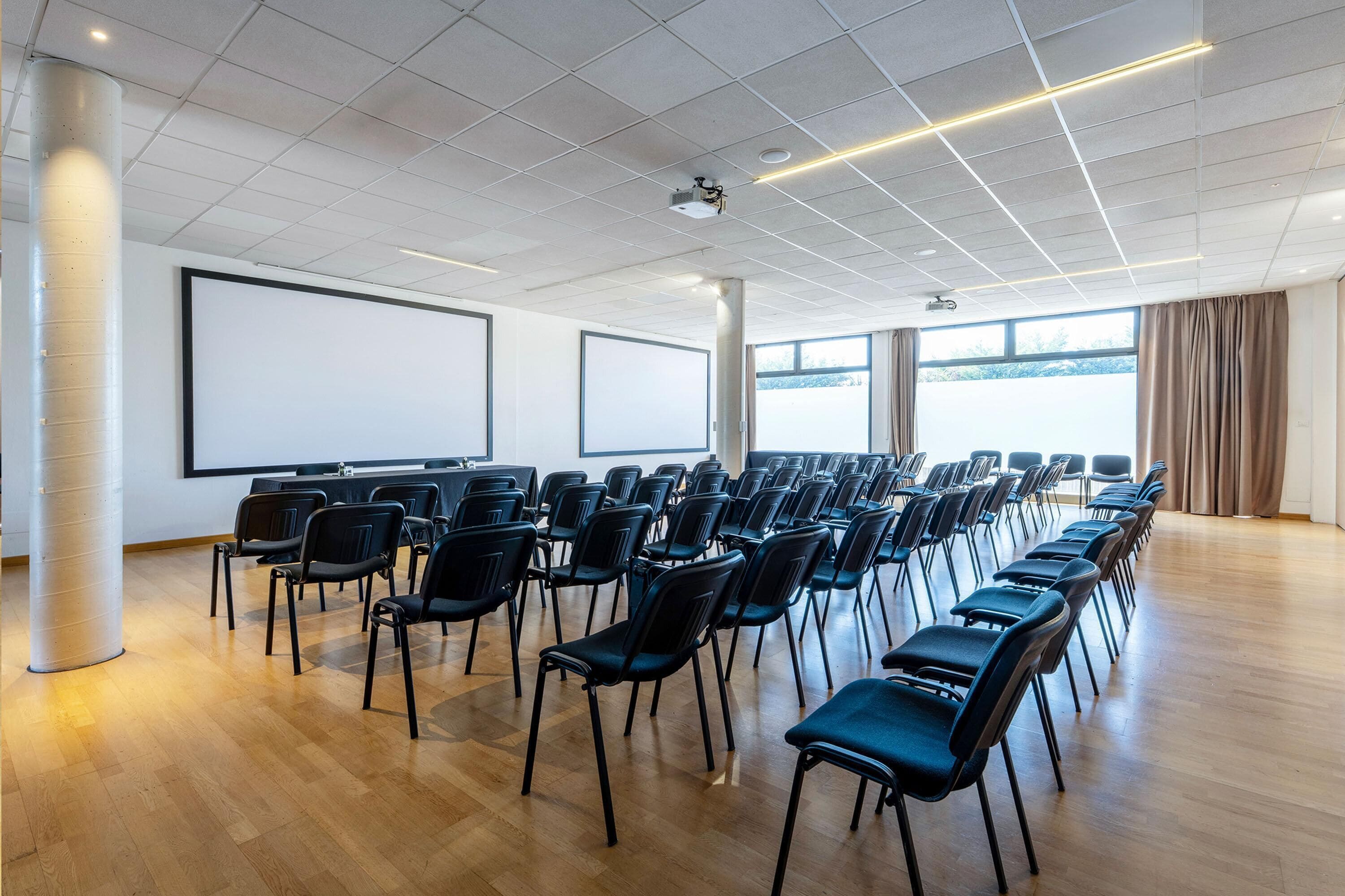 Une salle de conférence avec des rangées de chaises, un grand écran et un projecteur.