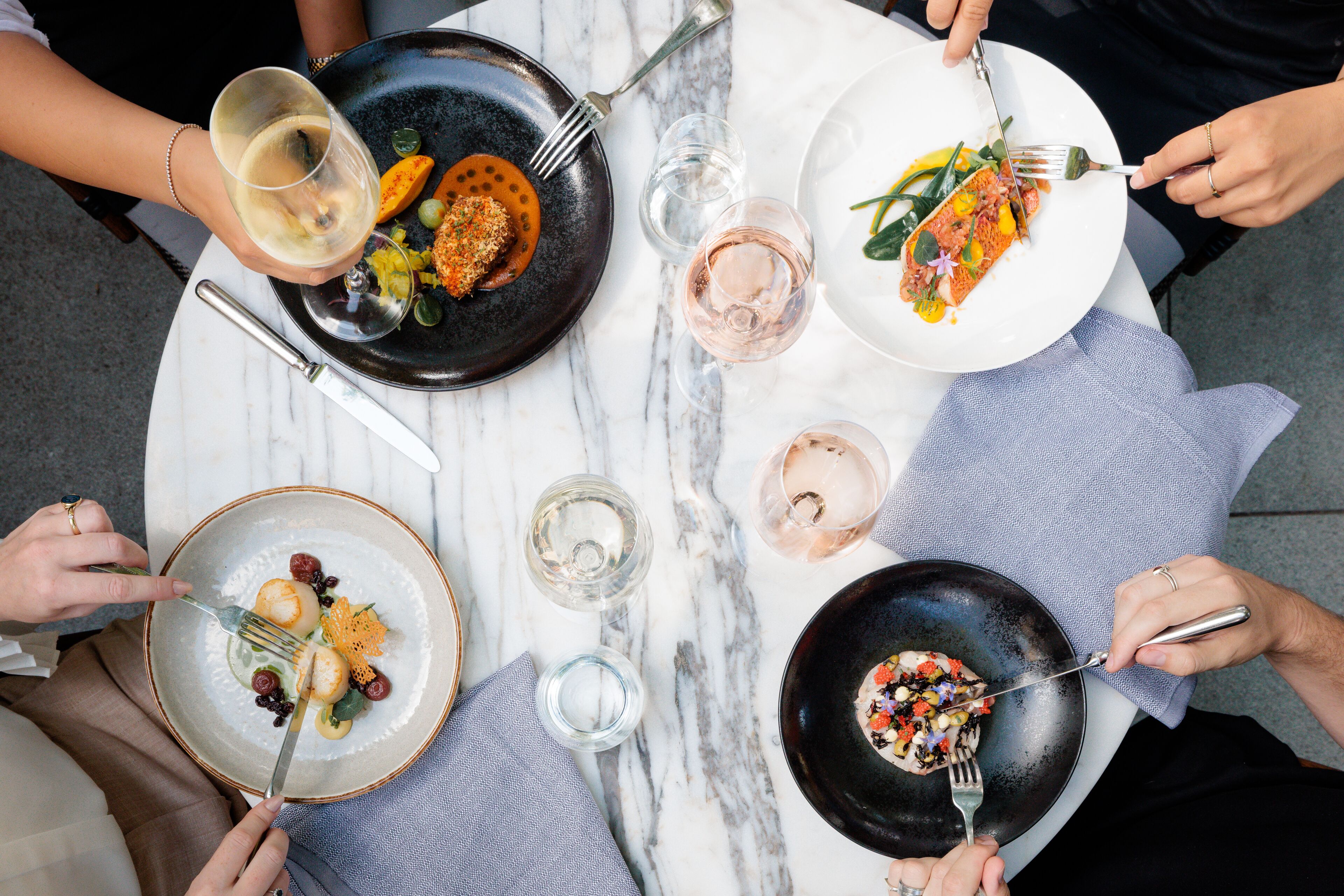 A round table with four plates of food, each accompanied by a fork and a glass of water.