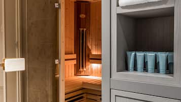 A modern bathroom with a wooden sauna, a glass shower enclosure, and neatly arranged toiletries.