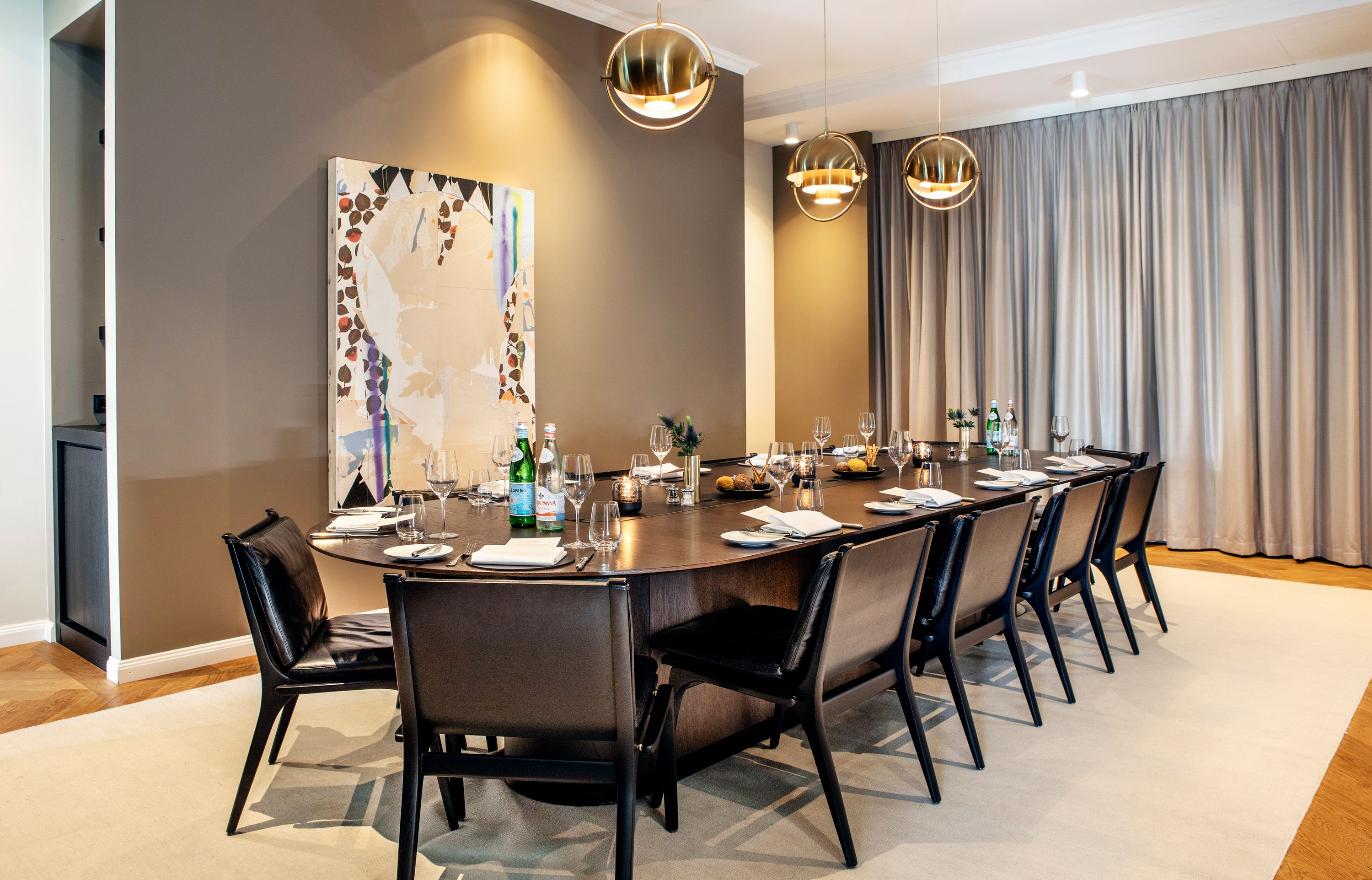 A modern dining room with a long table, black chairs, and a large abstract painting on the wall.