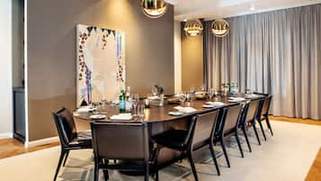 A modern dining room with a long table, black chairs, and a large abstract painting on the wall.