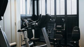 A gym with exercise equipment, including treadmills and stationary bikes, and large windows with blinds.
