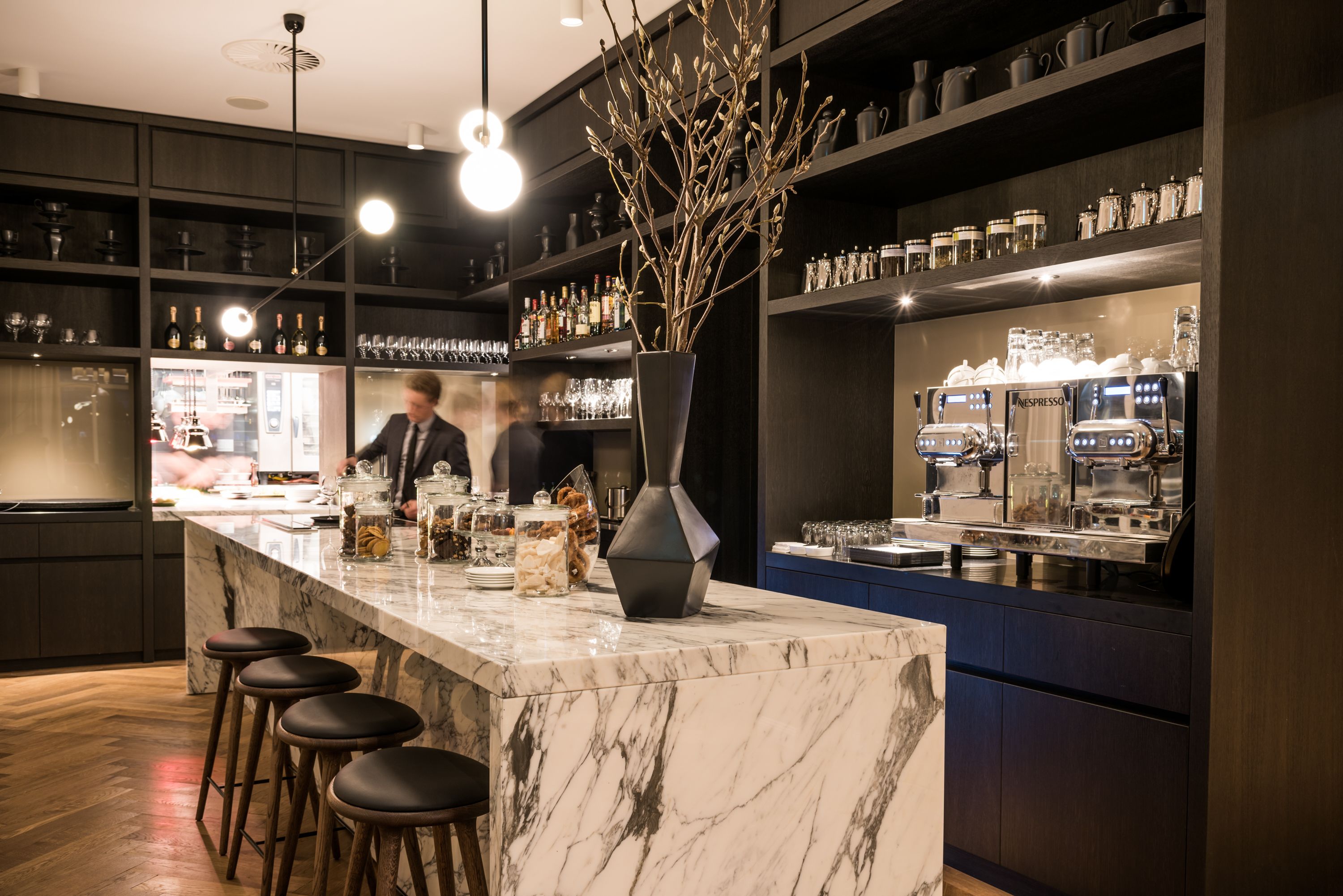 En moderne bar med en marmorplade, barstole og en vase med grene.
