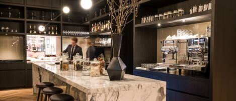 A modern bar area with a marble countertop, bar stools, and a vase with branches.