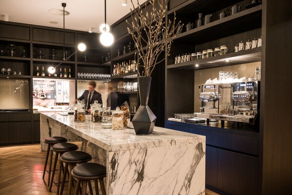 A modern bar area with a marble countertop, bar stools, and a vase with branches. - Pillows Grand Boutique Hotel Ter Borch Zwolle (Zwolle)