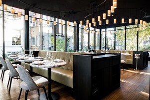 Ein modernes Restaurant mit einer zentralen Sitzinsel, großen Fenstern mit Blick auf die Stadt und Pendelleuchten.