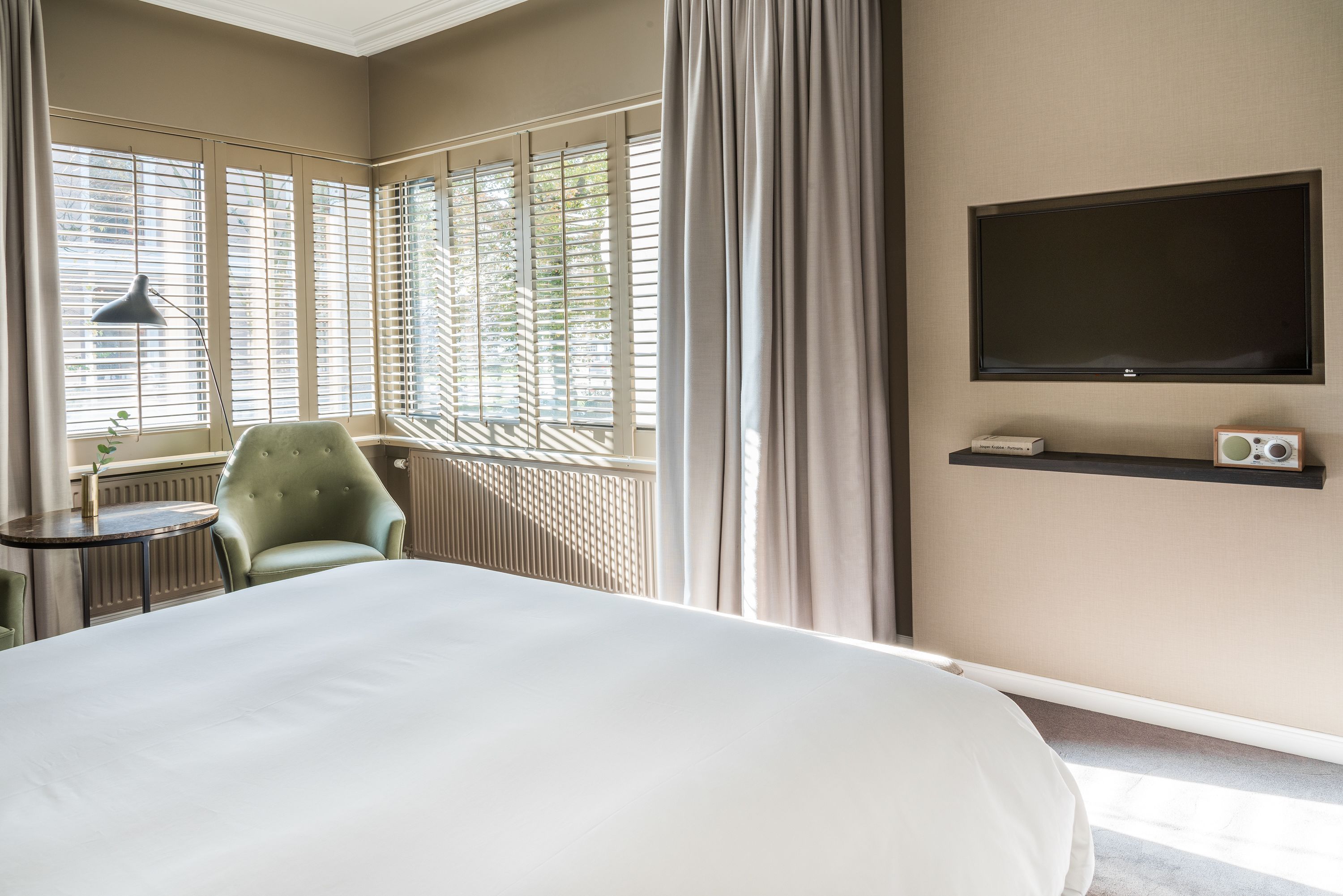 Una habitación de hotel con una cama grande, un sillón verde, una mesita, un televisor y una radio.