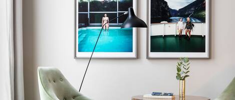Una sala de estar moderna con dos sillones verdes, una mesa redonda de centro y dos fotografías enmarcadas en la pared.