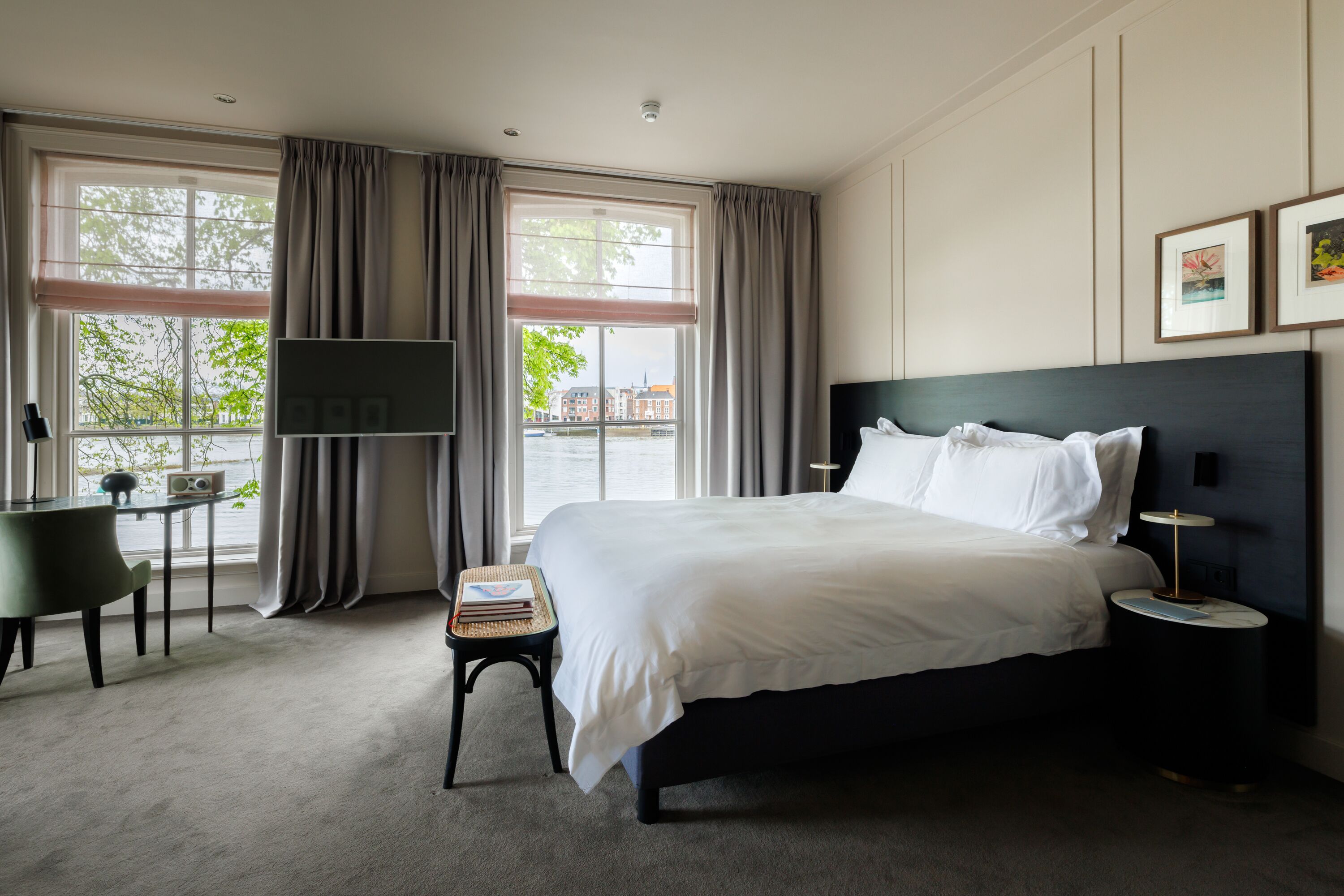 Habitación de hotel con una cama grande, un escritorio con silla, un televisor y vista a un edificio por la ventana.