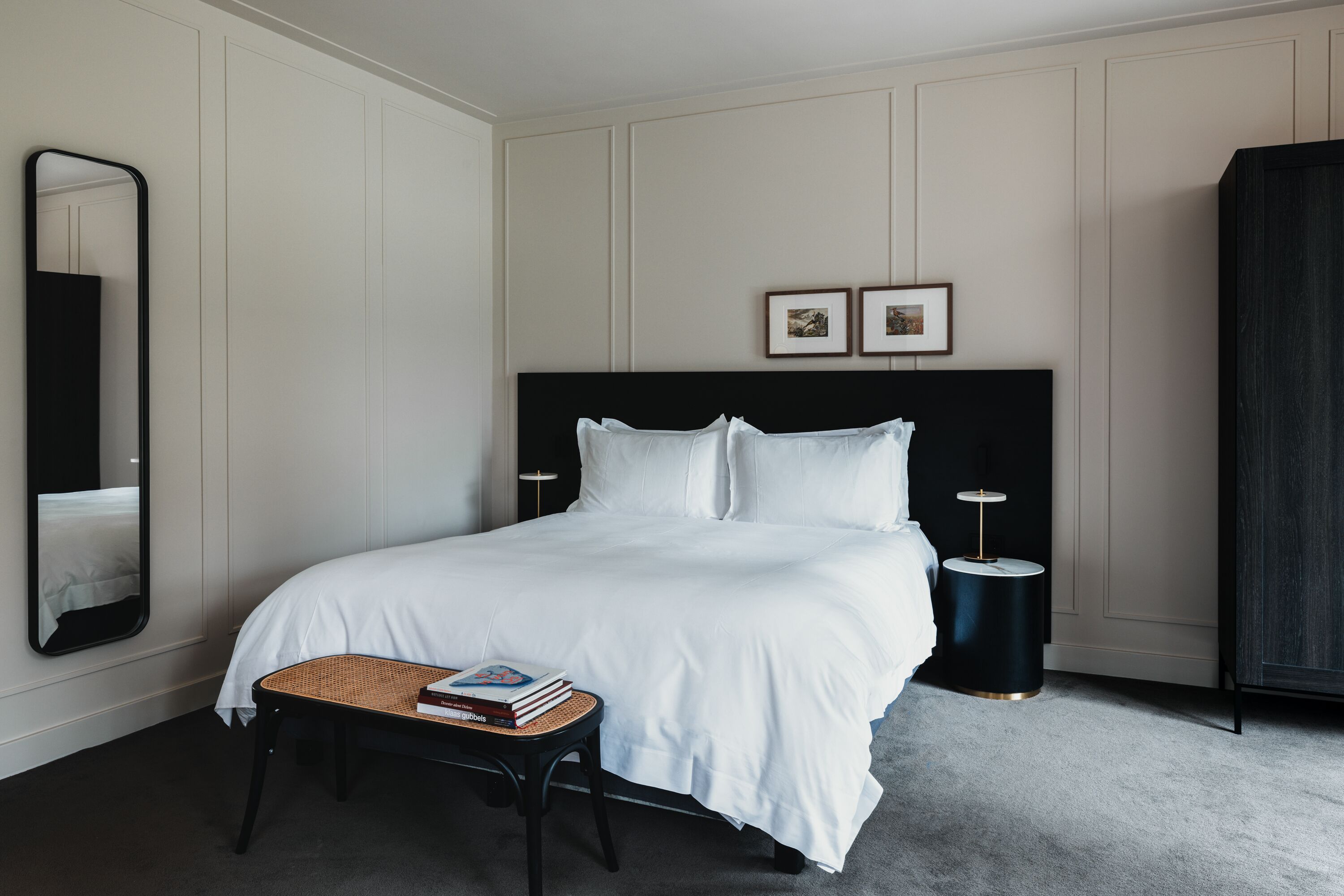 Een keurig ingerichte hotelkamer met een groot bed, een nachtkastje met boeken, een ronde tafel en een spiegel.