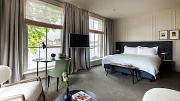 A hotel room with a large bed, a desk with a chair, a TV, and a view of the city.