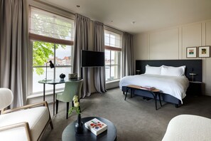 A hotel room with a large bed, a desk with a chair, a TV, and a view of the city.
