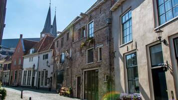 En brostensbelagt gade kantet af historiske bygninger, herunder en kirke med et tårn og et ur.