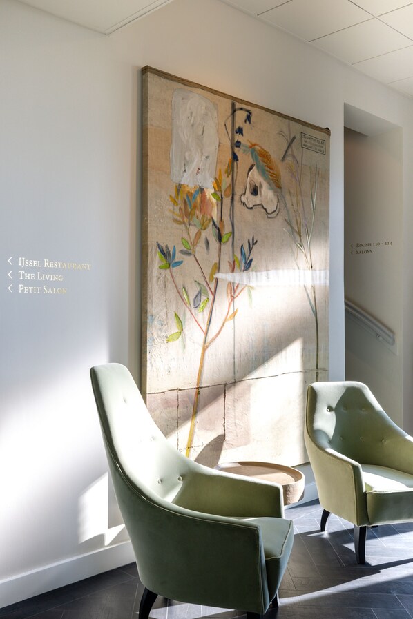 Un interior moderno con dos sillones verdes, un cuadro abstracto grande y un letrero en la pared que indica los números de habitación y la ubicación de los salones.