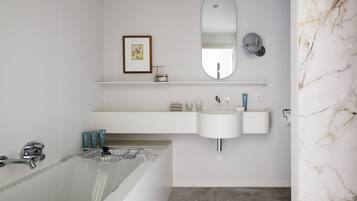 A modern bathroom with a bathtub, two sinks, a large mirror, and a marble wall.