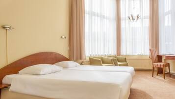 Habitación de hotel con una cama grande, un escritorio y una silla. Cuenta con una ventana con cortinas y un candelabro.