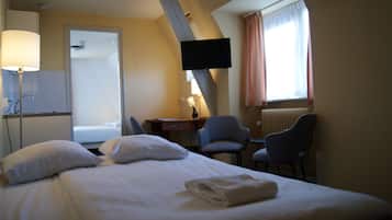 Ett hotellrum med en säng, ett skrivbord, två stolar, en TV och ett fönster med gardiner.