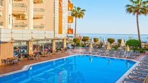 A hotel pool area with lounge chairs and umbrellas, a clear view of the sea, and a building with balconies. - Monart City Hotel - All Inclusive (Alanya)