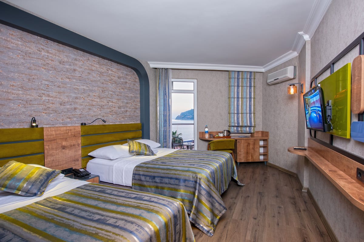 A hotel room with two beds, a desk, a TV, and a window with a view.