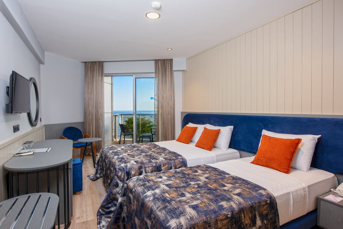 A hotel room with two beds, a desk, a chair, and a TV.