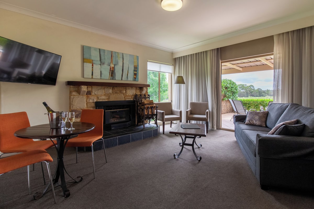 A living room with a stone fireplace, a flat-screen TV, a sofa, and a dining area with chairs.