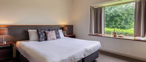 Une chambre d’hôtel avec un grand lit, deux tables de chevet, une fenêtre avec des rideaux et une vue sur la verdure.