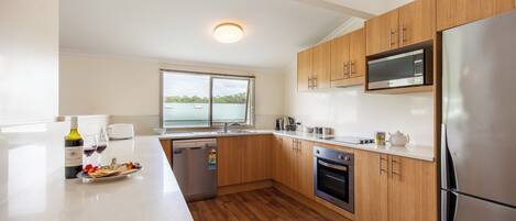 A modern kitchen with wooden cabinets, stainless steel appliances, and a large window.