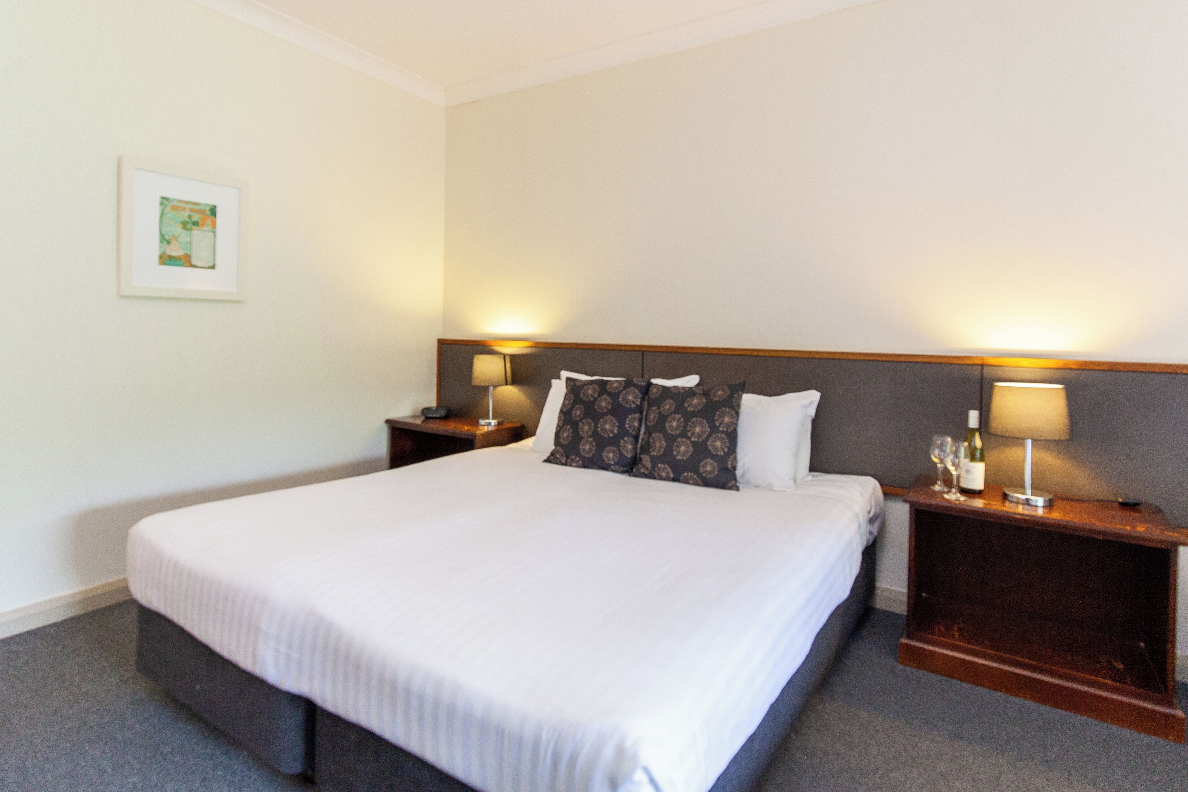 A neatly made bed with a white comforter, two bedside tables with lamps, and a framed picture on the wall.