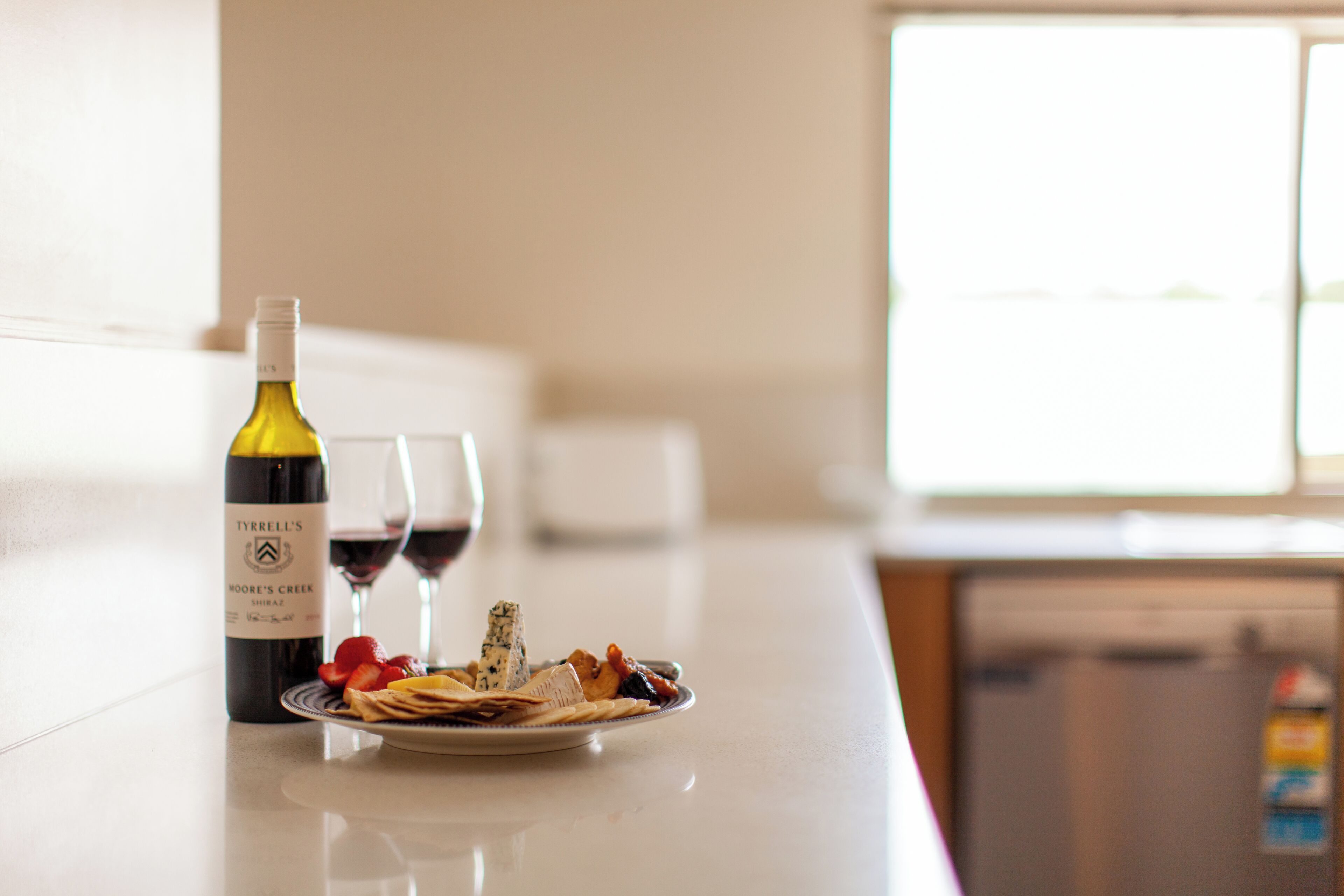 A kitchen counter with a bottle of wine, a glass of red wine, and a plate of food.
