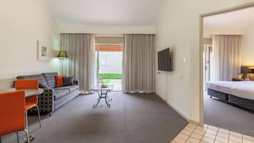Quarto de hotel com sofá, mesa, televisão e cama.