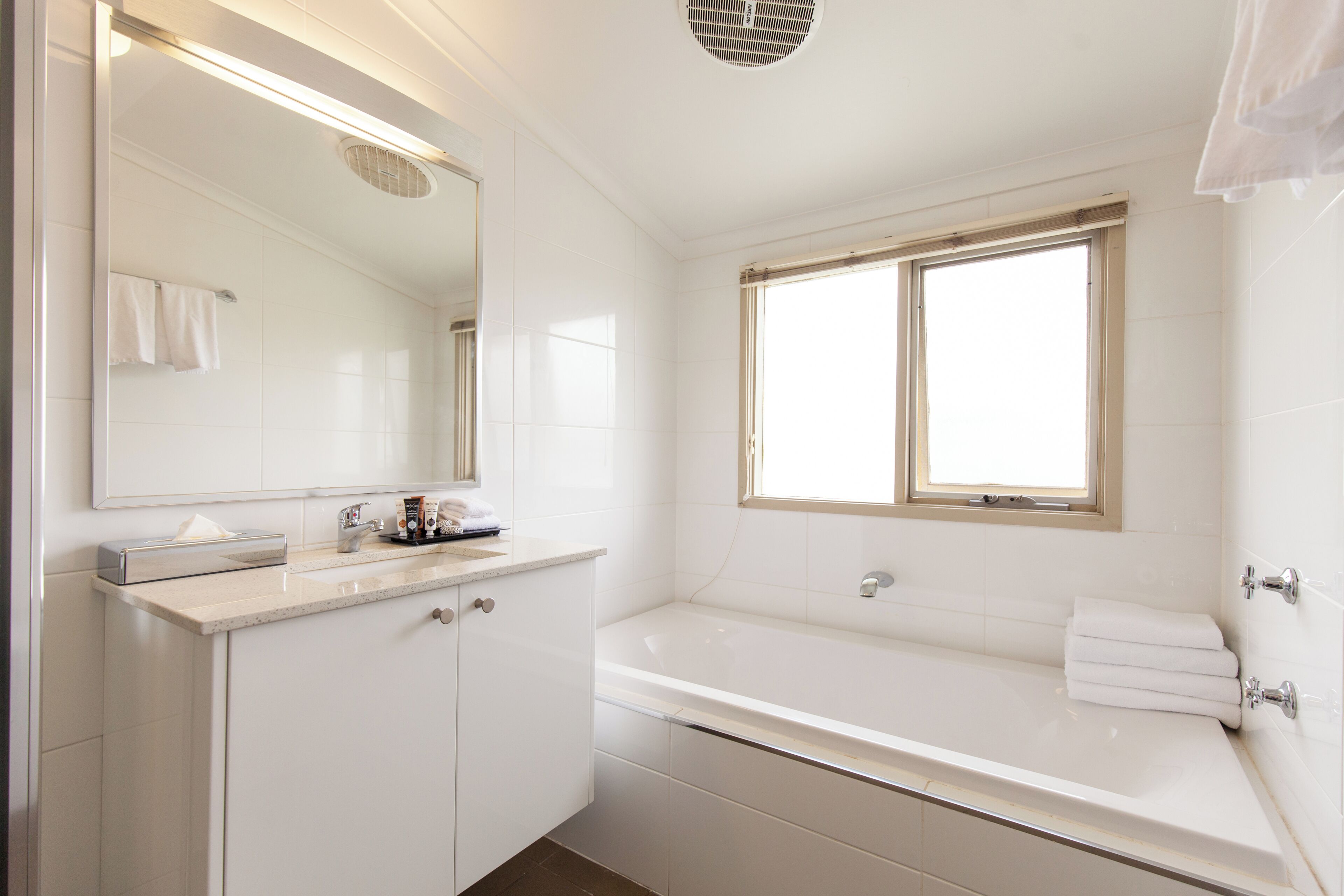 A modern bathroom with a large mirror, a bathtub, and a window.