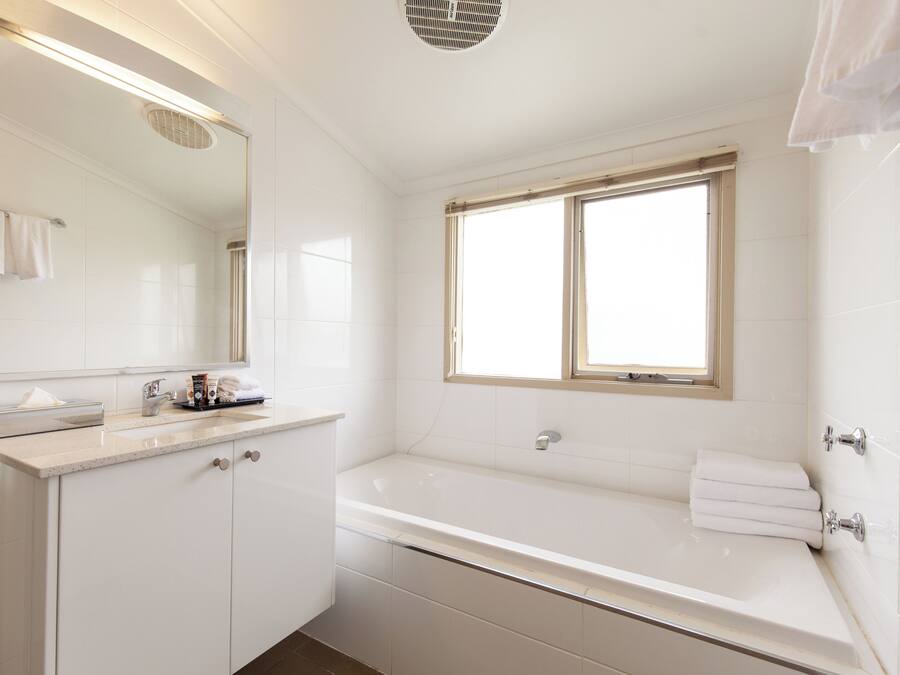 A modern bathroom with a large mirror, a bathtub, and a window.