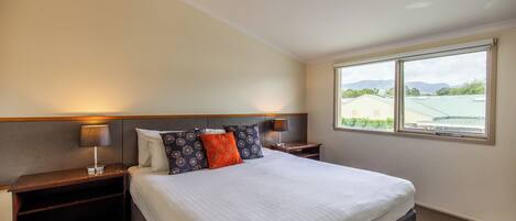 Habitación de hotel con una cama grande, dos mesitas de noche, una lámpara de techo y una ventana con vistas a edificios y montañas.
