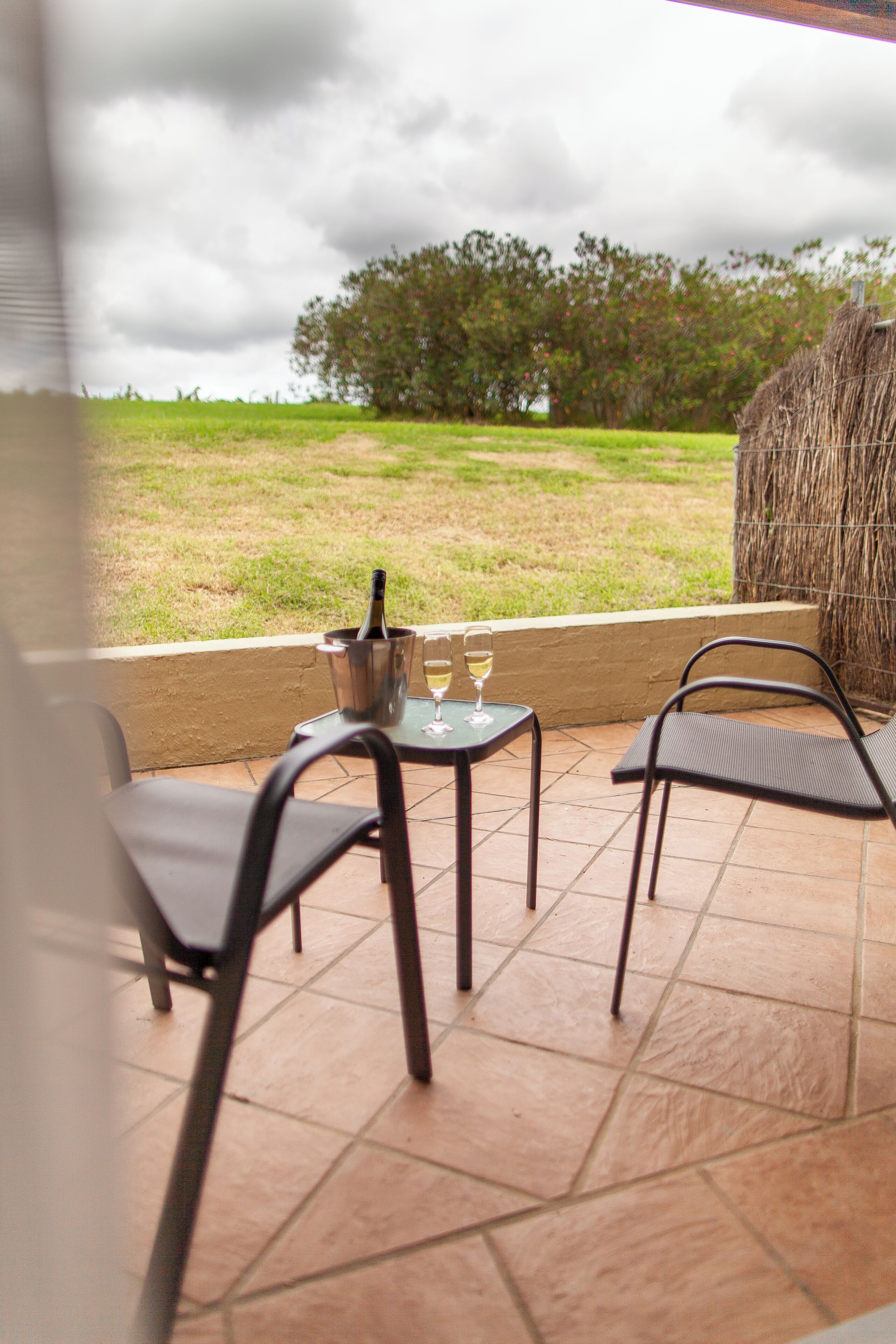 Une terrasse avec deux chaises et une table, une bouteille de champagne et un verre de vin.