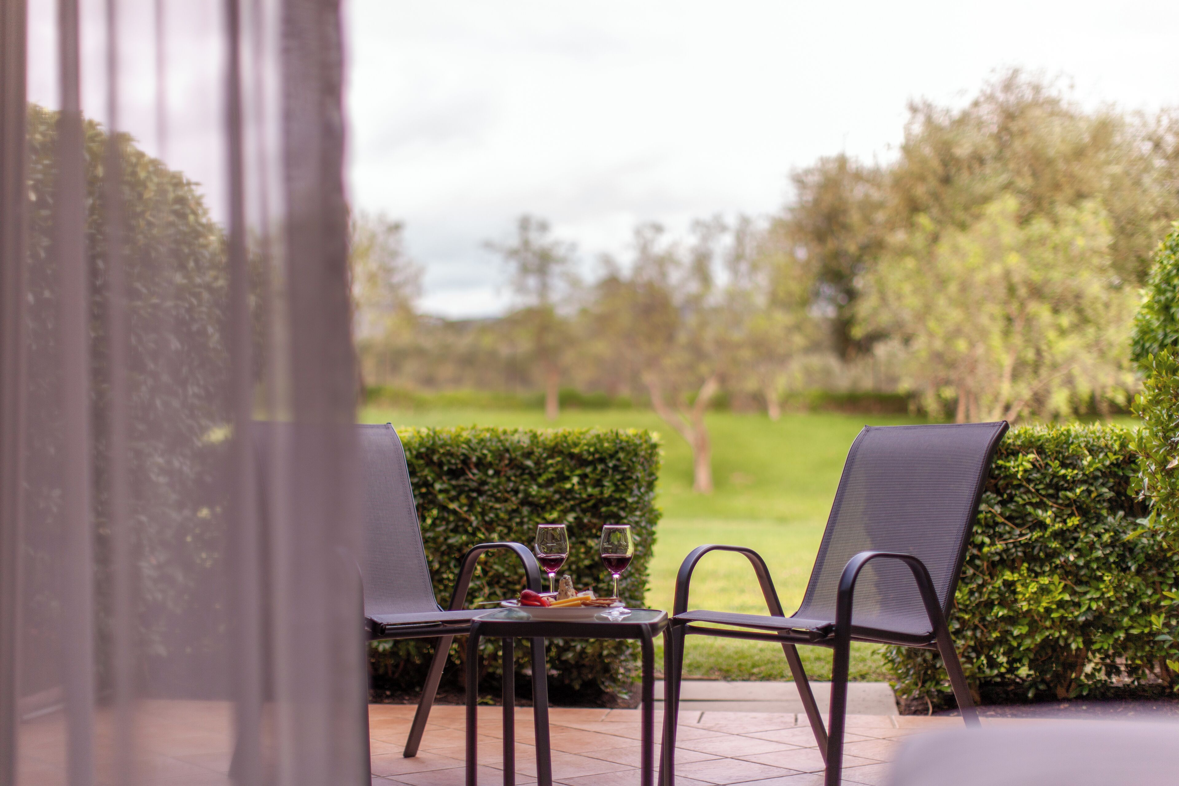An outdoor seating area with two chairs and a table, two glasses of wine, and a small plate of food.