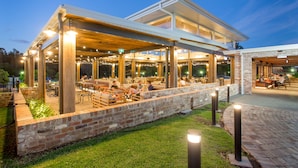 An outdoor restaurant with a covered seating area, brick walls, and a grassy lawn. - Harrigan's Hunter Valley (Pokolbin)