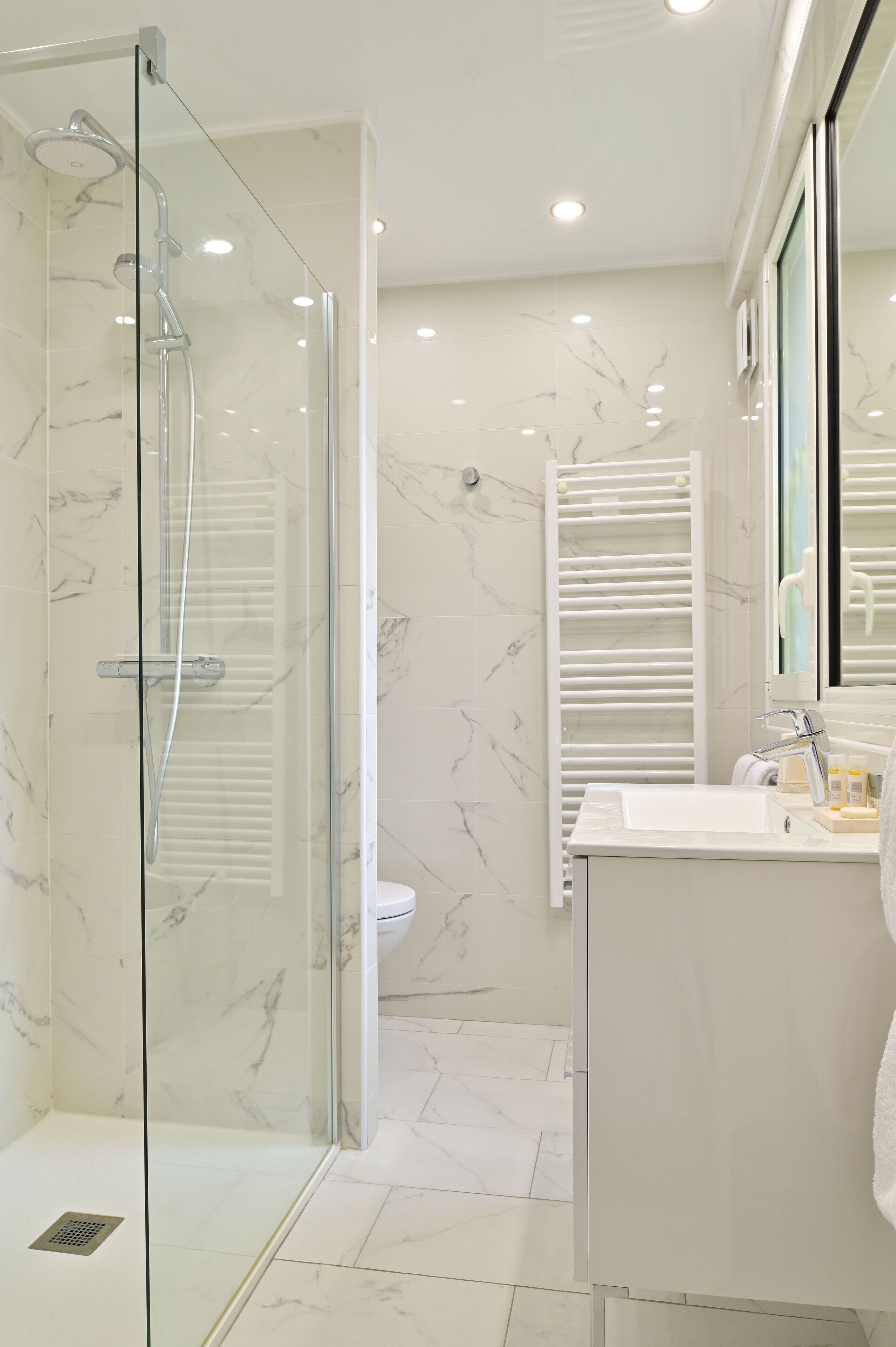 A modern bathroom with a glass-enclosed shower, a white sink, and a marble-tiled floor.