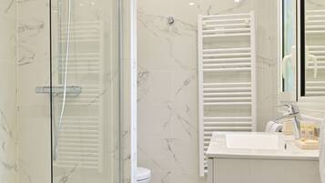 A modern bathroom with a glass-enclosed shower, a white sink, and a marble-tiled floor.
