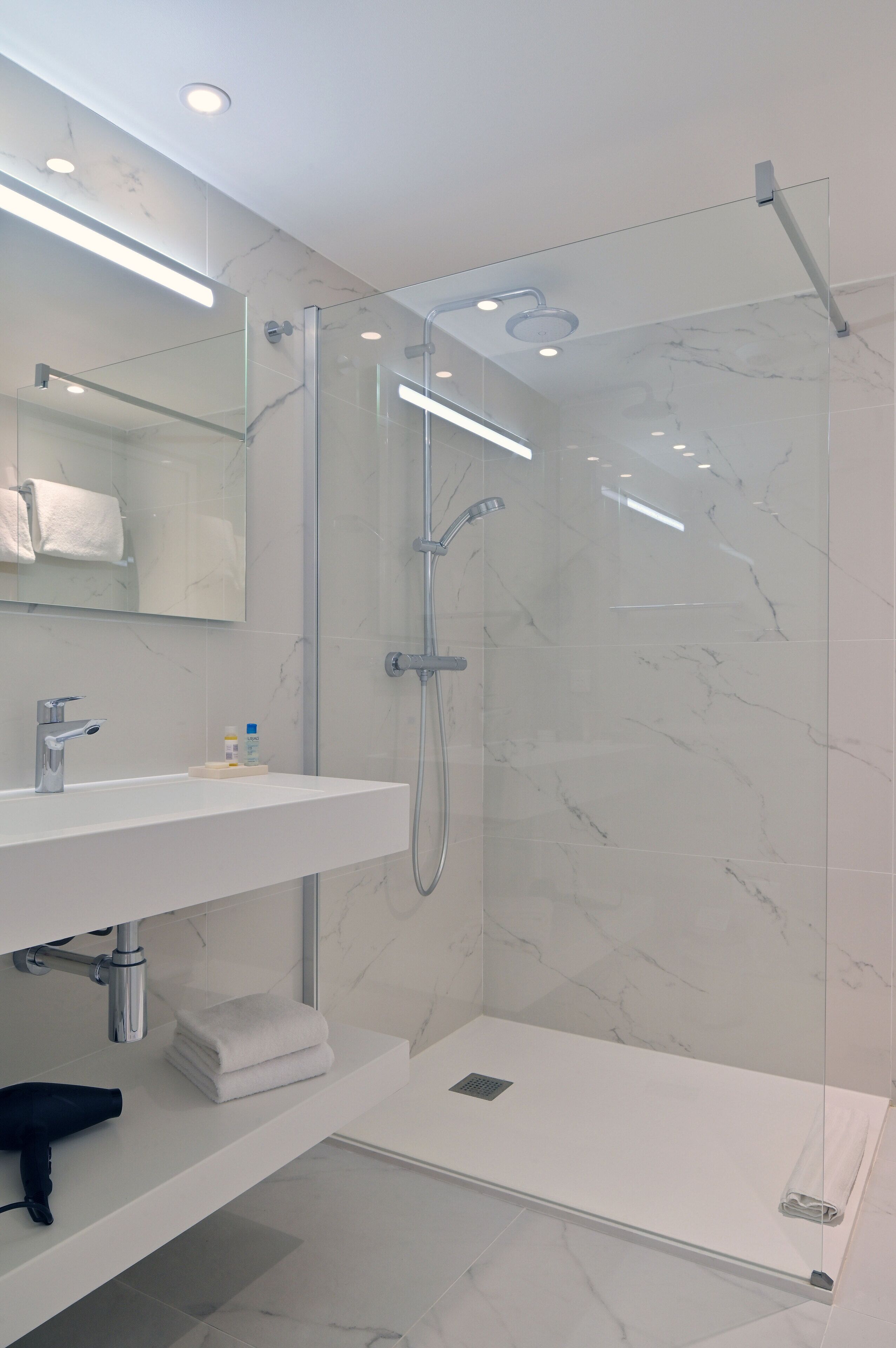 Un baño moderno con ducha de vidrio, un lavabo blanco con espejo y suelo de mármol.