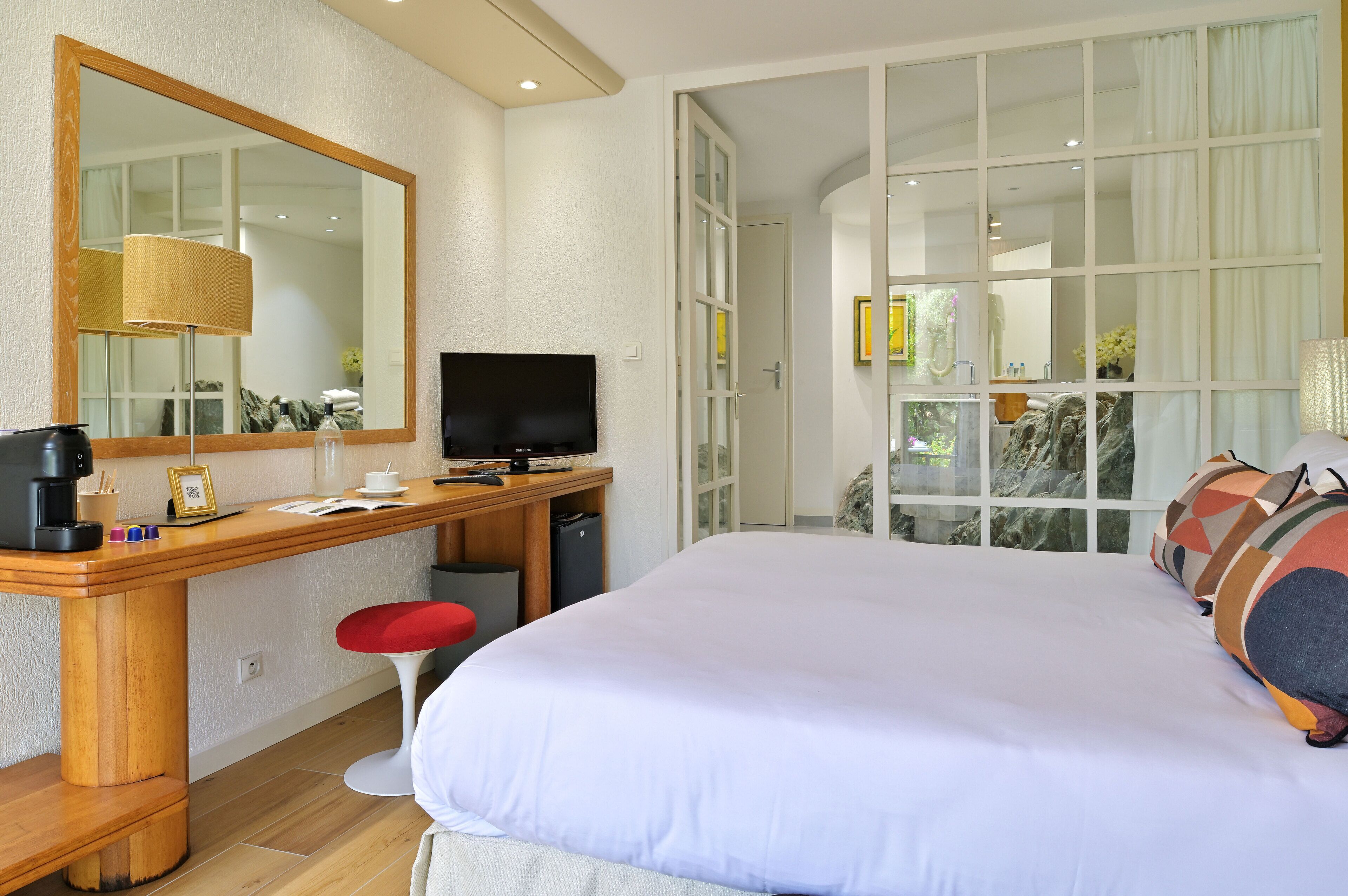 A hotel room with a large bed, a desk with a TV, a mirror, and a window with curtains.
