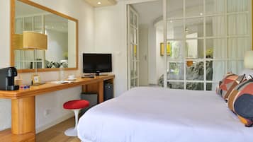 A hotel room with a large bed, a desk with a TV, a mirror, and a window with curtains.