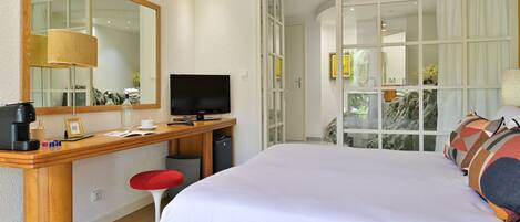 Une chambre d’hôtel avec un grand lit, un bureau avec une télévision, un miroir et une fenêtre avec des rideaux.