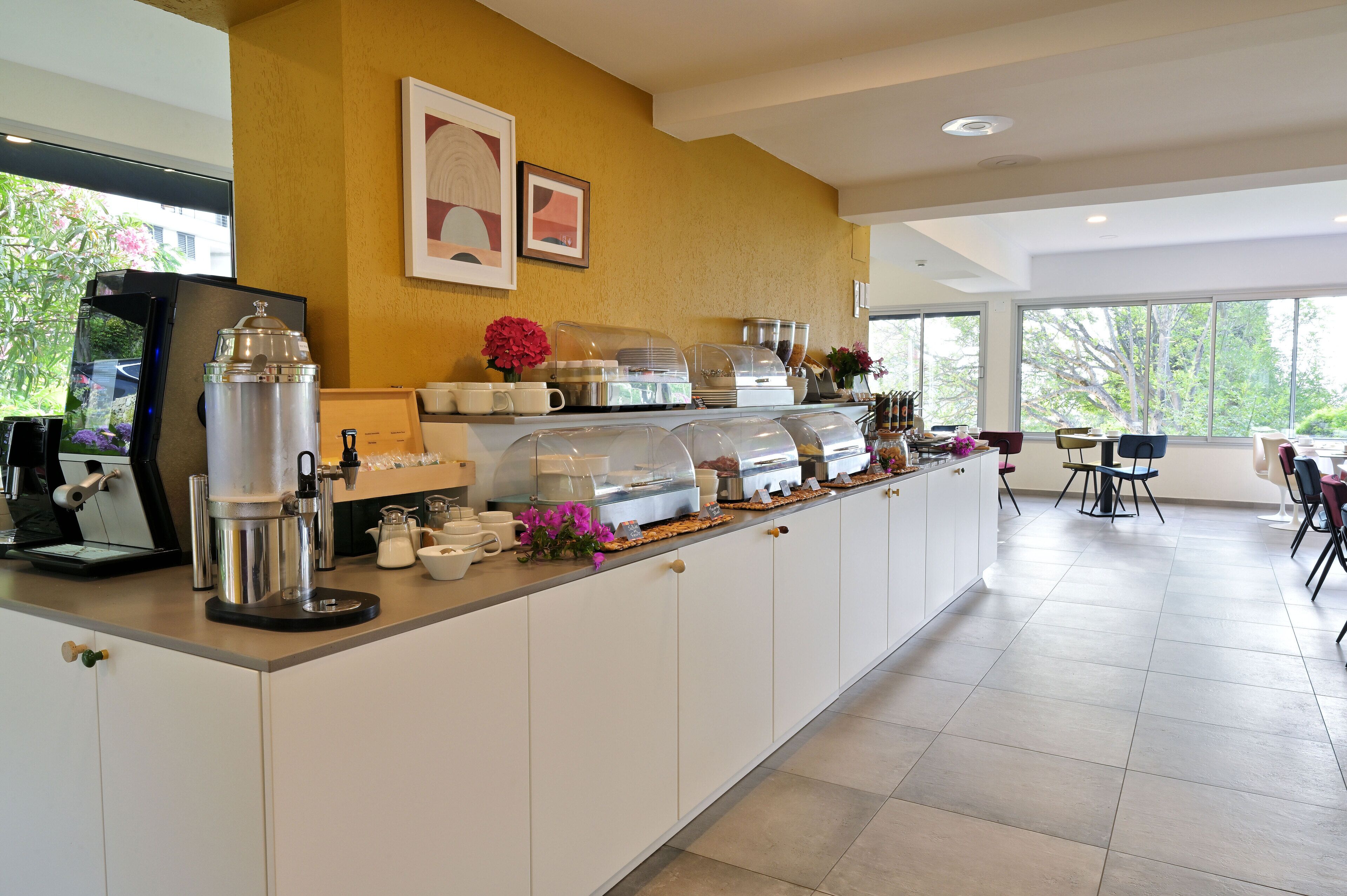 A modern kitchen with a coffee station, white cabinets, and large windows.