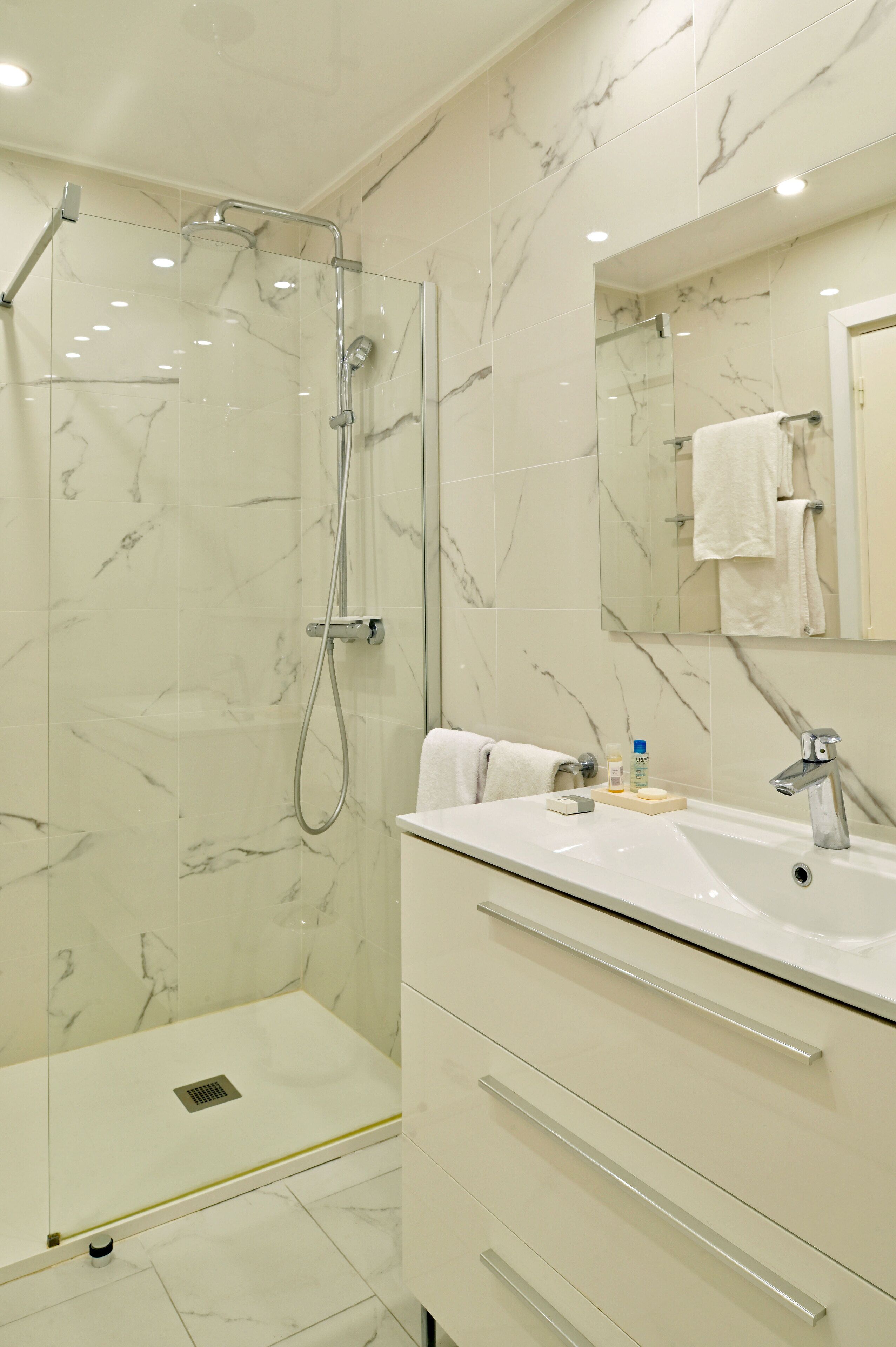A modern bathroom with a glass-enclosed shower, a white sink, and a marble-tiled wall.