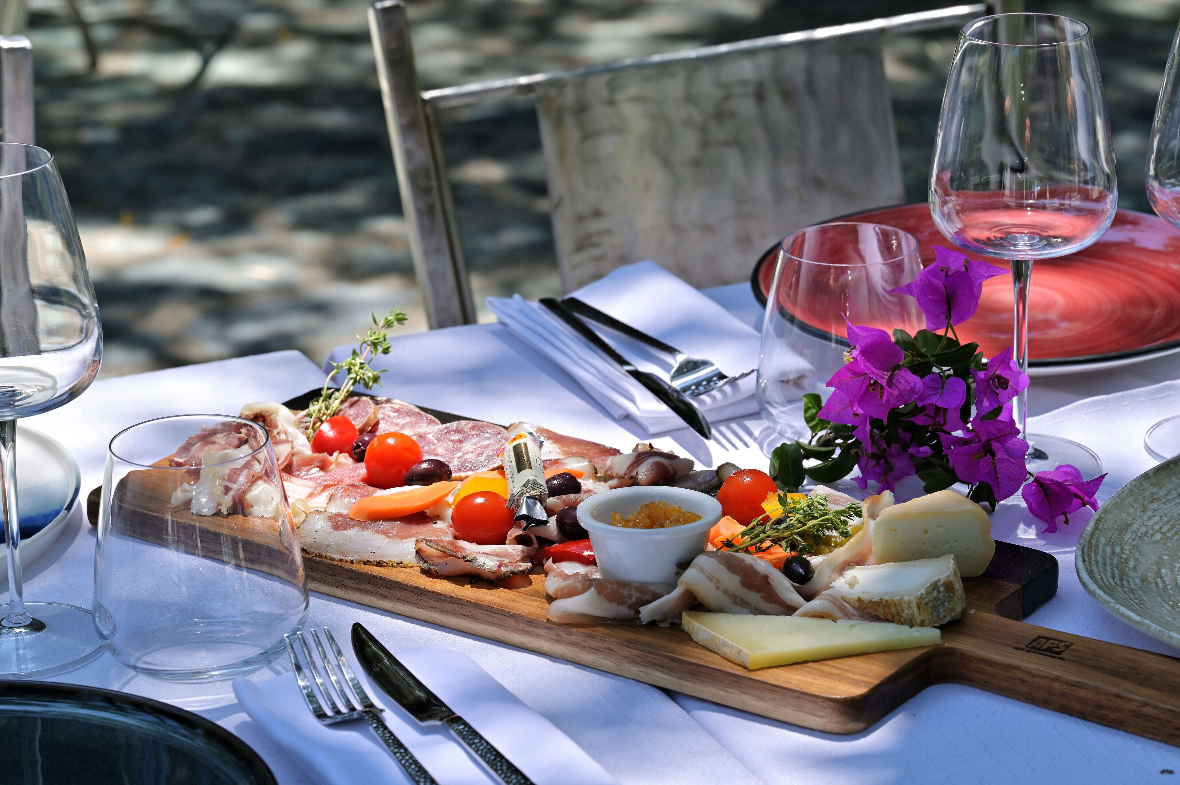 A table set with a charcuterie board, wine glasses, and a vase of purple flowers.