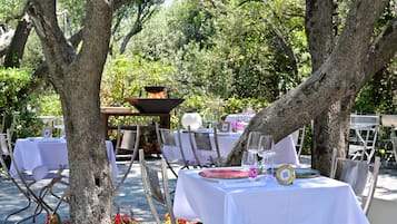 Un espace extérieur aménagé pour les repas, avec des tables disposées sous les arbres, le tout entouré de verdure.