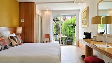 Habitación de hotel con una cama grande, cabecero de madera, escritorio con lámpara y vista a un jardín a través de una puerta corrediza de vidrio.