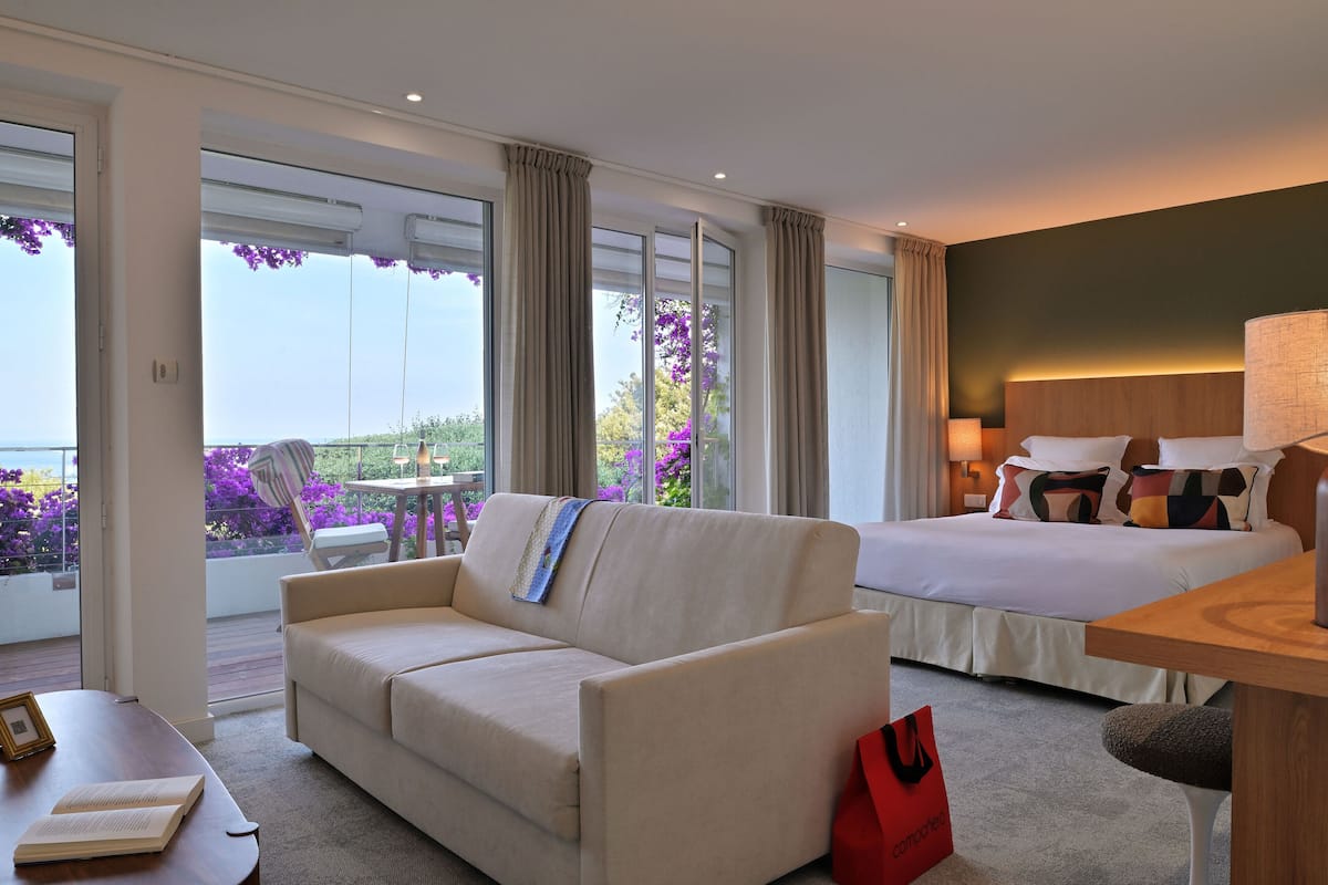 Habitación de hotel con sofá, cama, mesa y vista al exterior.