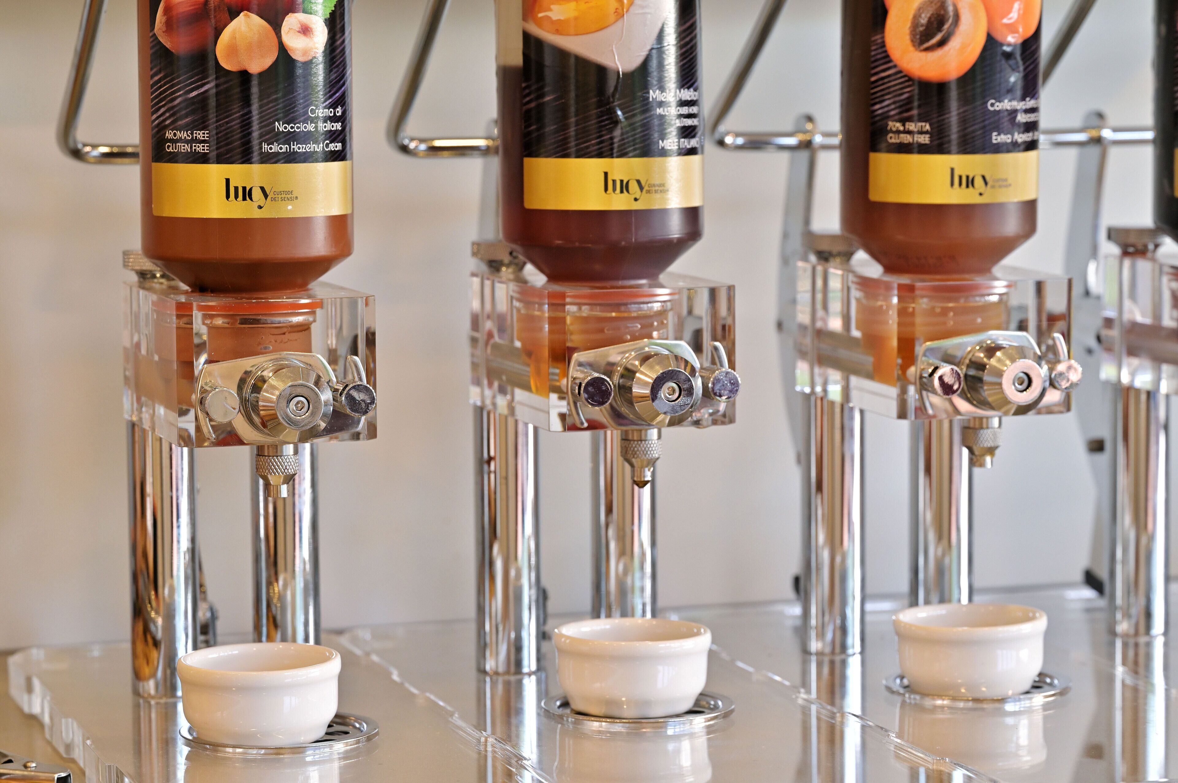 Tre erogatori per condimenti con etichette, ognuno con una piccola ciotola sottostante.